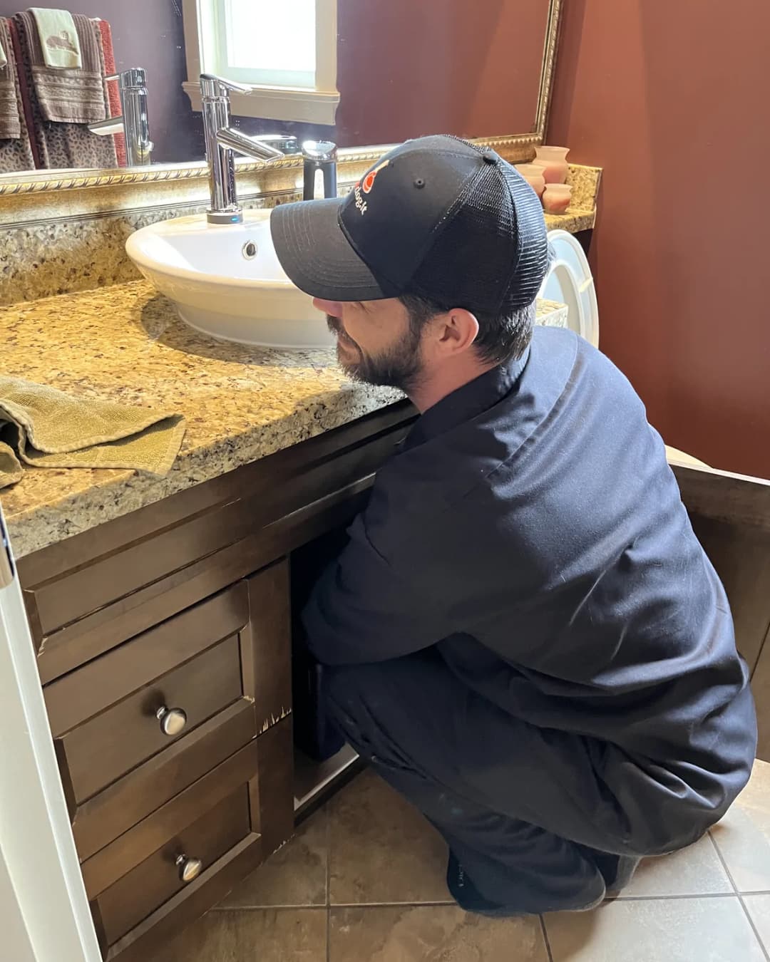 Technician working on accessible plumbing beneath a bathroom sink