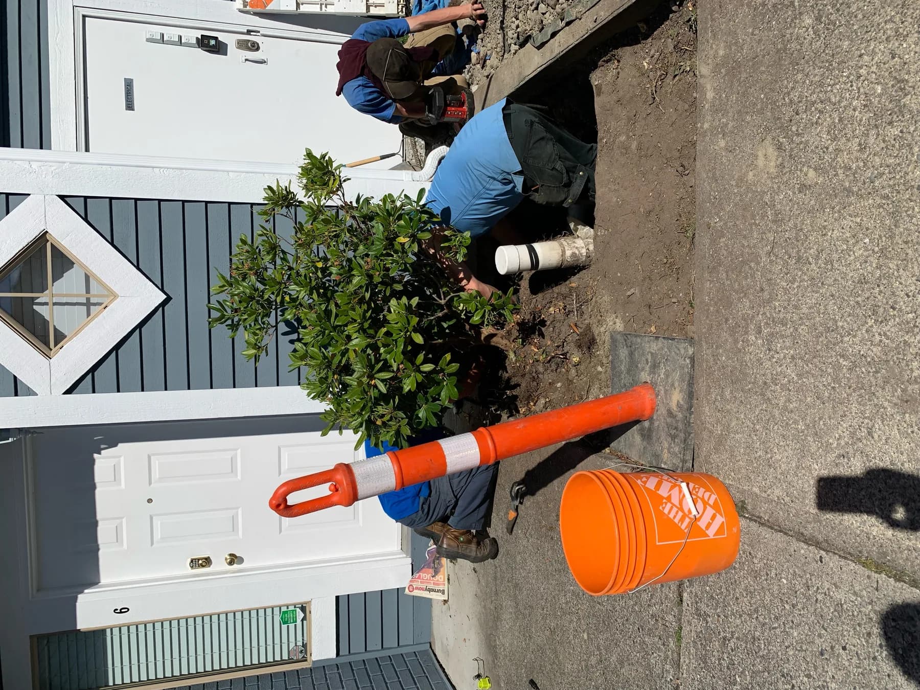 Field crew working at an exterior plumbing excavation beside a residential property