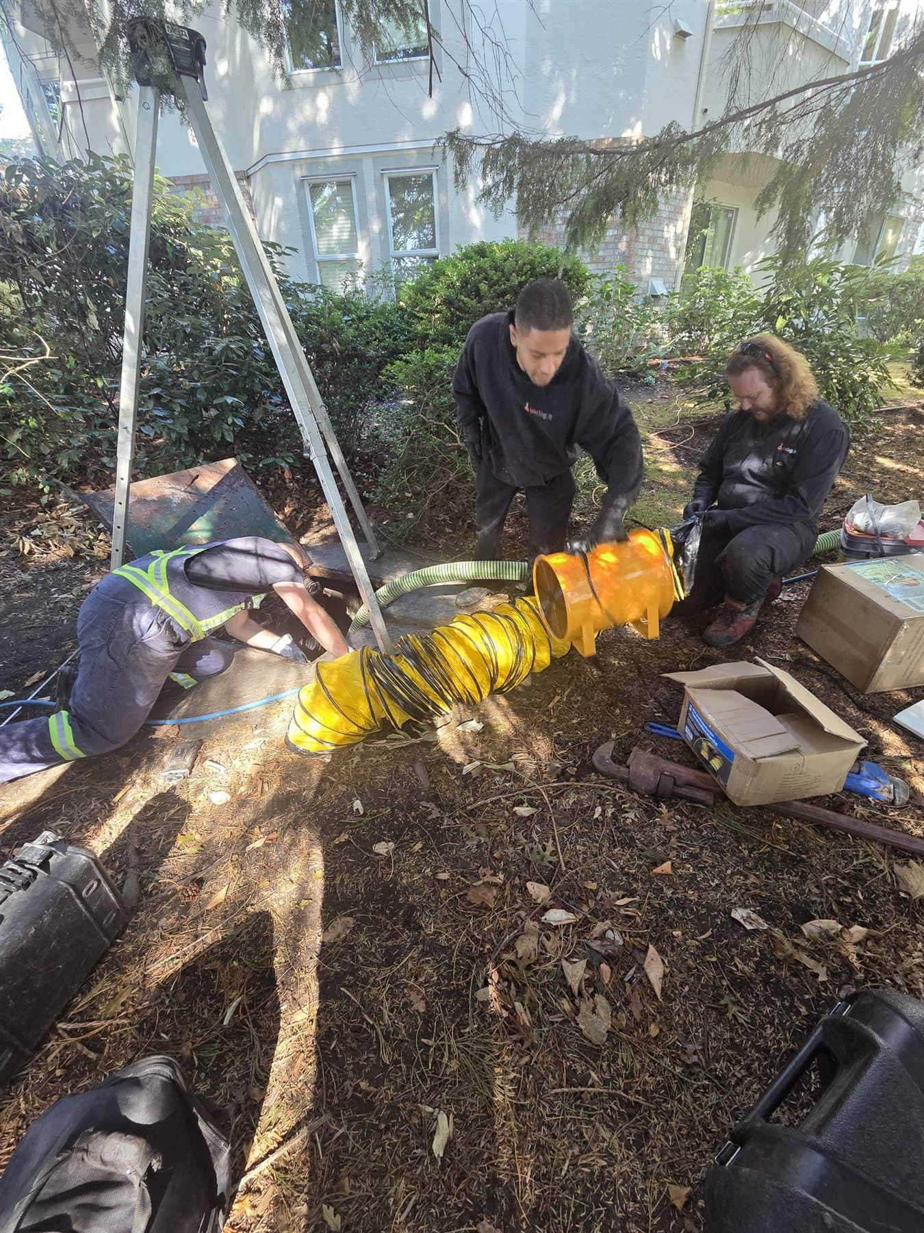 Technicians setting up ventilation and retrieval equipment at an open sump-pump vault