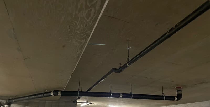 Newly installed supported storm-drain pipe running through a multi-unit parkade