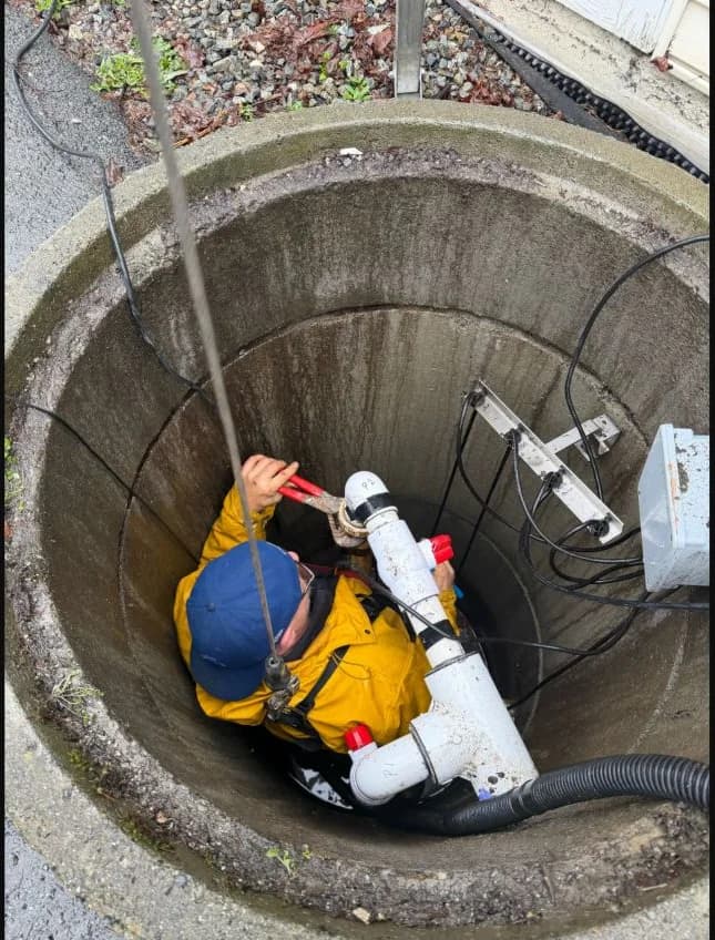 Technician working inside an open storm-sump station during pump removal